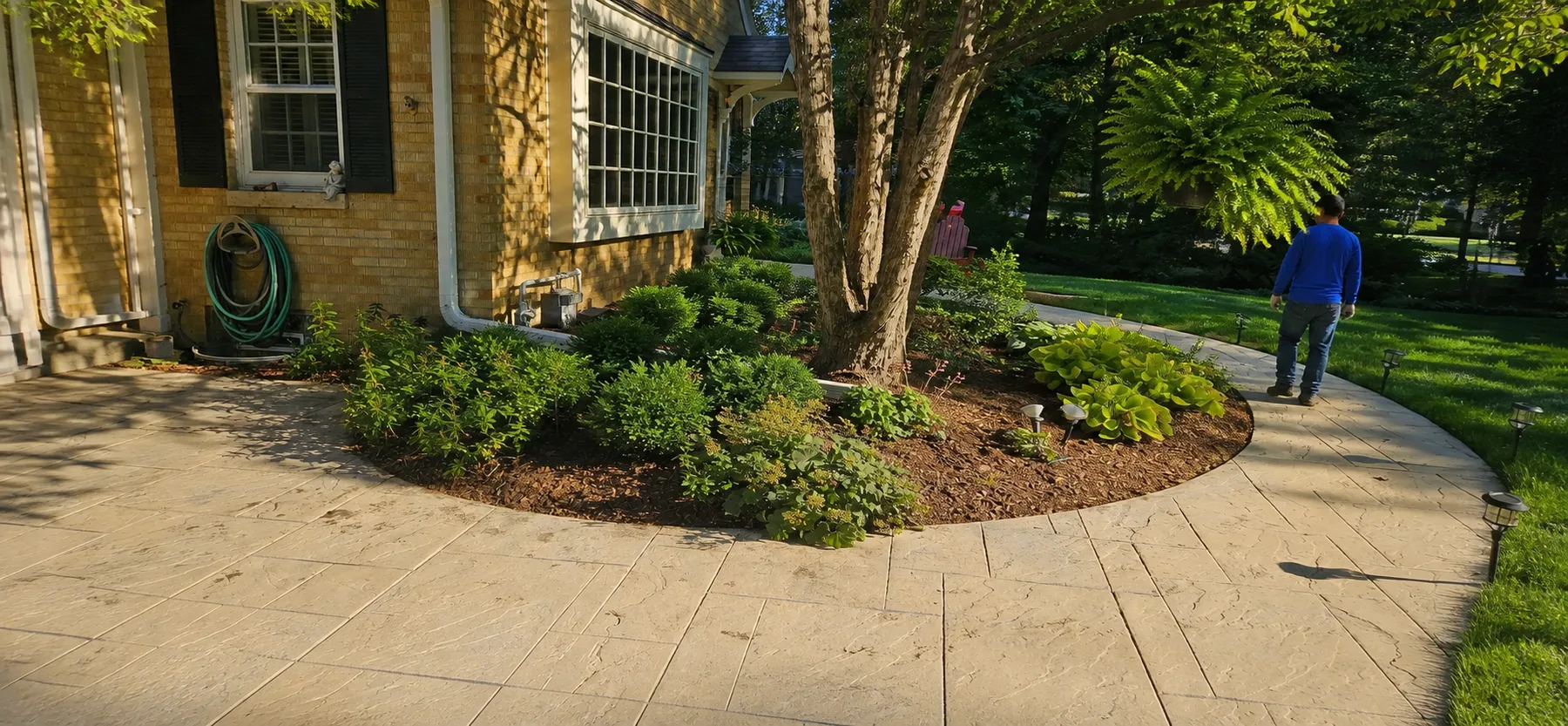 Anonymous blue-uniform team member inspecting a finished residential walkway and planting bed