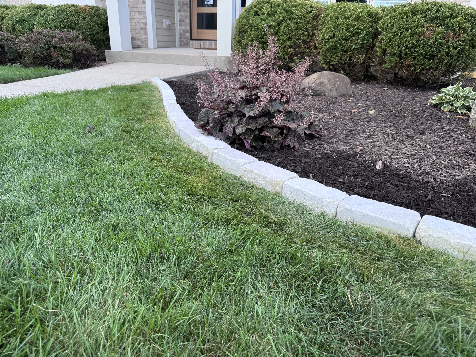 Close-up of a pale stone border separating lawn from a mulched planting bed