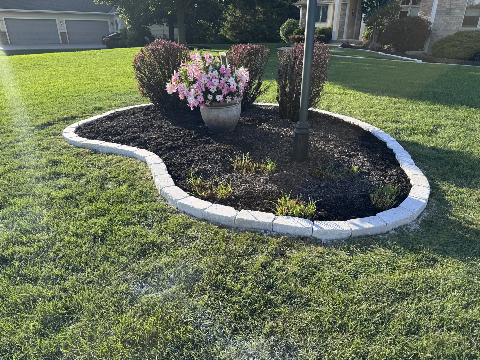 Curved pale stone border around a finished mulched island planting bed