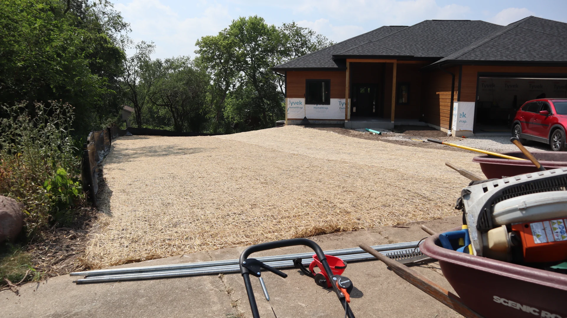 Straw-covered prepared front lawn beside a house with unfinished exterior areas