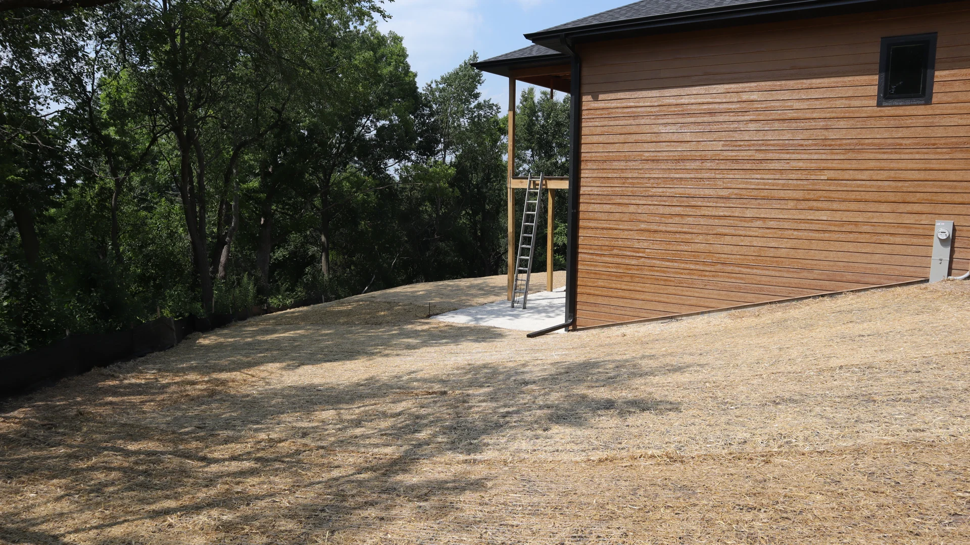 Protective straw over prepared sloped ground beside a wood-sided house